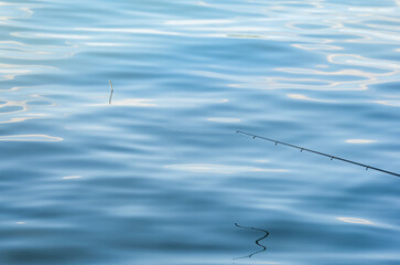 A monofilament fishing line on a fishing rod ring against blue water. Fishing loat or bobber at the surface of the water.