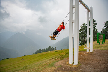 Gravity-Defying Joy: Man on Swing in Orange T-Shirt