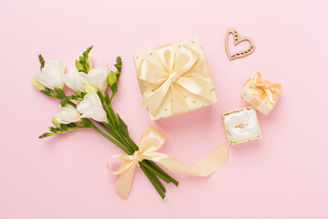 White fresia flower and gift box with diamond ring on color background, top view