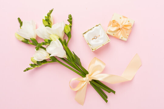 White fresia flower and gift box with diamond ring on color background, top view