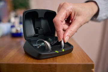 Close Up Of Person Picking Up Wireless Hearing Aid Or Device From Charging Case At Home - obrazy, fototapety, plakaty
