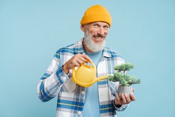 Gray haired man wearing stylish shirt, holding flower pot watering it with yellow watering can © Maria Vitkovska