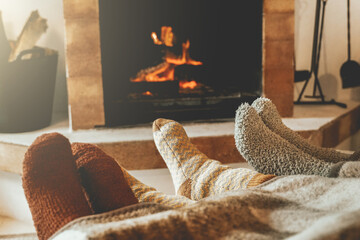 Family resting feet by fireplace on fall or winter time. People warming feet with blanket and socks...