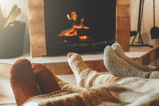 Family resting feet by fireplace on fall or winter time. People warming feet with blanket and socks by cozy fire.