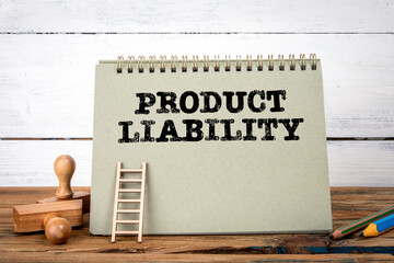 PRODUCT LIABILITY. Green notepad on wooden texture table and white background
