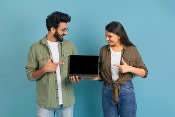 Loving eastern couple showing laptop with black empty screen
