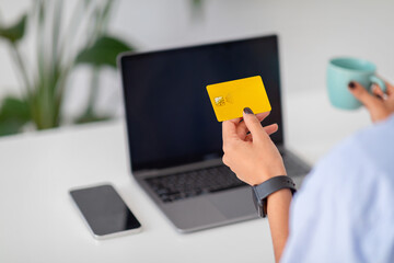 Focused on yellow credit card in hand on laptop screen, online shopping or banking