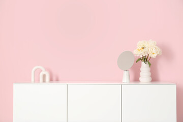 Vase with white peonies and mirror on dresser near pink wall in room