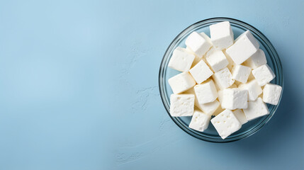Cubes of feta cheese in glass bowl on blue background. Top view, copy space