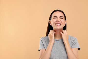 Suffering from allergy. Young woman scratching her neck on beige background, space for text