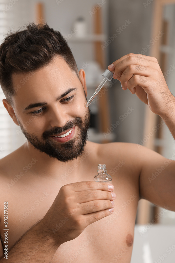 Poster Handsome man applying cosmetic serum onto his face in bathroom