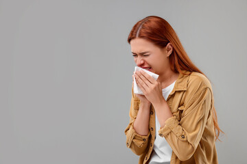 Suffering from allergy. Young woman with tissue sneezing on grey background, space for text