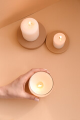 Woman holding burning candle on pale orange background