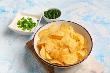 Bowls of tasty sour cream with sliced green onion and potato chips on blue background