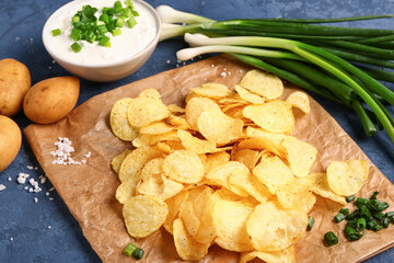 Bowl of tasty sour cream with sliced green onion and potato chips on blue background