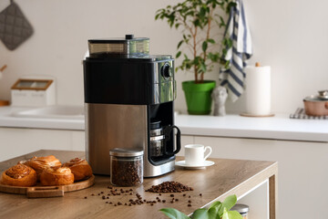 Modern coffee machine with jar of roasted beans, cup and buns on table in kitchen