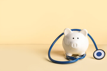 Piggy bank with stethoscope on beige background