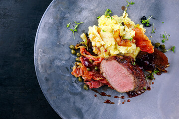 Traditional fried wild hare back filet with plums, capers and potato salad in red wine jus served as top view on Nordic design plate with copy space right © HLPhoto