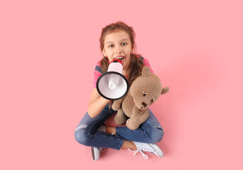 Little girl with megaphone and teddy bear sitting on pink background