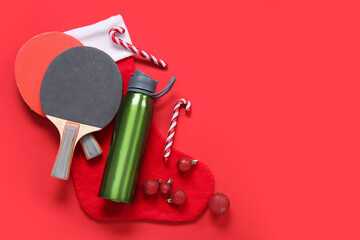 Composition with sports bottle, ping pong rackets and Christmas decorations on red background