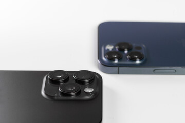 two smartphone cameras on a white background, Iphone 15 pro max Black Titanium, iphone 12 pro max