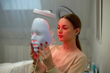 Beautiful young woman getting a led light therapy mask treatment for her face