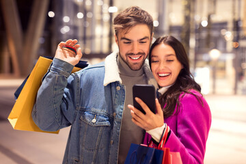 Spouses in winter attire using cellphone application for shopping outdoor