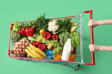 Woman pushing shopping cart full of food on green background