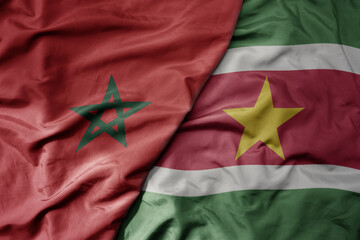 big waving national colorful flag of suriname and national flag of morocco .