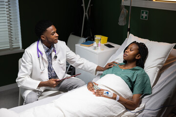 African female patient lying in a hospital bed is attentively listening to a young African doctor...