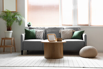 Interior of light living room with grey sofa, houseplants and wooden coffee table