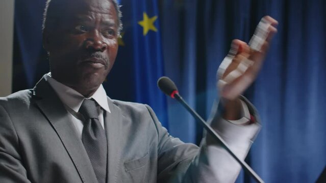 African American senator speaking in mic and gesturing with hand while making public announcement on press conference, EU and US flags in backgroundAfrican American senator speaking in mic and gesturi