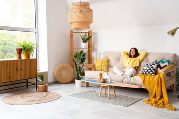 Pretty young woman sitting on white sofa in light living room