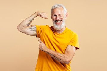 Portrait of middle aged man wearing yellow t shirt showing biceps, pointing finger at tattooed hand