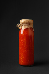 Hot sauce made from chili peppers, paprika, tomatoes and garlic in a jar on a black background.