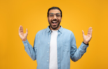 Surprised and joyful man with beard and glasses raises his hands in excitement - obrazy, fototapety, plakaty