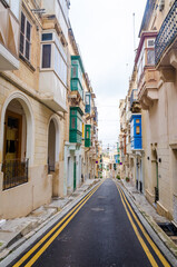 Fototapeta na wymiar Old medieval street with yellow buildings, beautiful balconies and flower pots in Birgu, Valletta, Malta with nobody