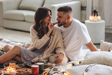 Concept of lazy weekend in bed or romantic home holiday celebration: christmas, new year, saint Valentine's Day. Beautiful young loving couple enjoy time together, embracing, kissing, having fun - obrazy, fototapety, plakaty