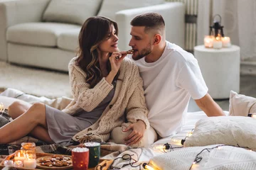 Fotobehang Concept of lazy weekend in bed or romantic home holiday celebration: christmas, new year, saint Valentine's Day. Beautiful young loving couple enjoy time together, embracing, kissing, having fun © ArtSys