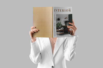 Elegant young woman reading interior magazine on light background