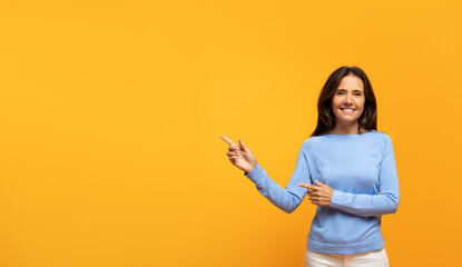 Cheerful old european woman in blue sweater gestures with both hands to right - obrazy, fototapety, plakaty
