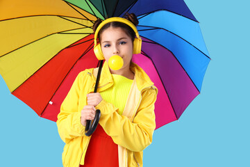 Trendy girl with umbrella blowing bubble gum on blue background