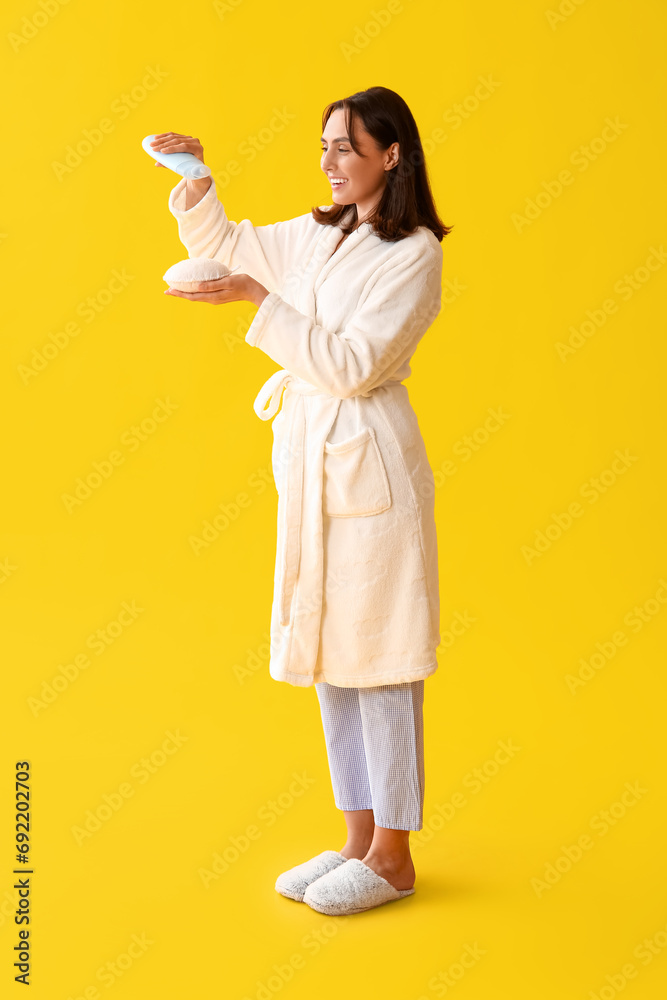 Sticker Young woman in bathrobe with shower gel and loofah on yellow background