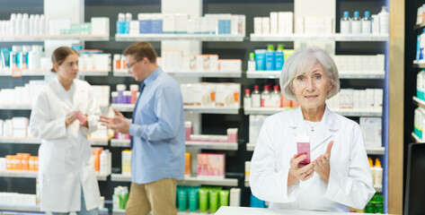 In pharmacy, senior female specialist holds in hands and presents shows new effective remedy for...