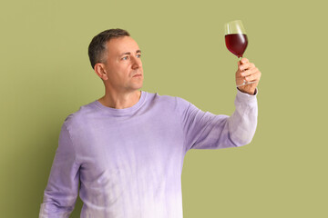 Mature man with glass of red wine on green background