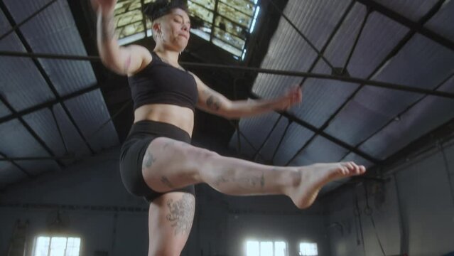 Young strong female athlete with tattooed body doing one-legged squat exercise on balance trainer ball during gym workout