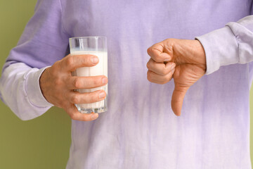 Mature man with glass of milk showing thumb-down on green background, closeup