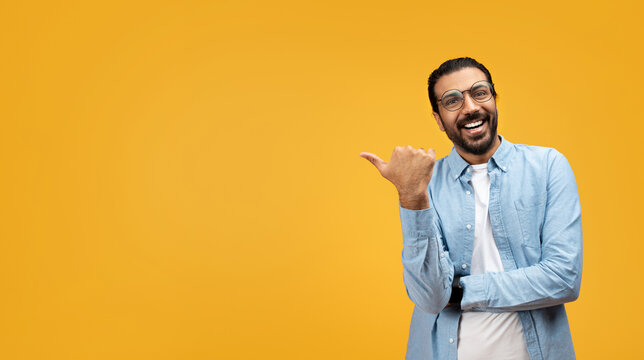 Laughing man in a blue shirt pointing to his left with a thumbs-up gesture