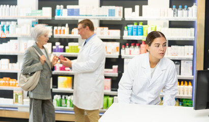 Girl pharmacist in pharmacy works with computer, searches among nomenclature of drugs, specifies price and availability of medicine
