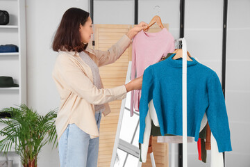 Young woman choosing new clothes in shop - obrazy, fototapety, plakaty